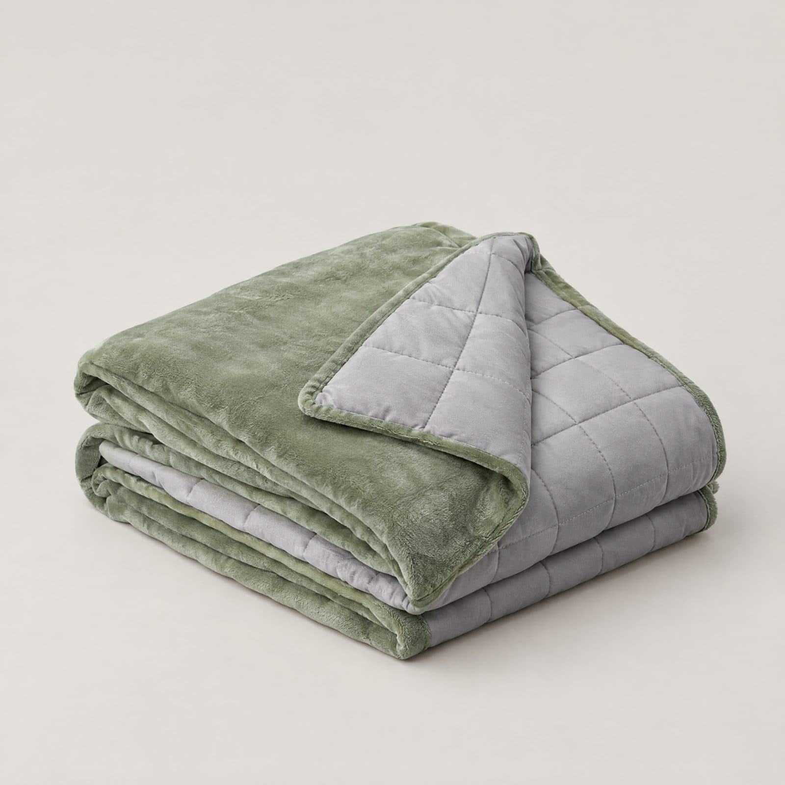 Couette lestée pliée dont un coin retourné montre ses deux faces, velours vert sauge et lyocell gris clair surpiqué, sur fond gris clair
